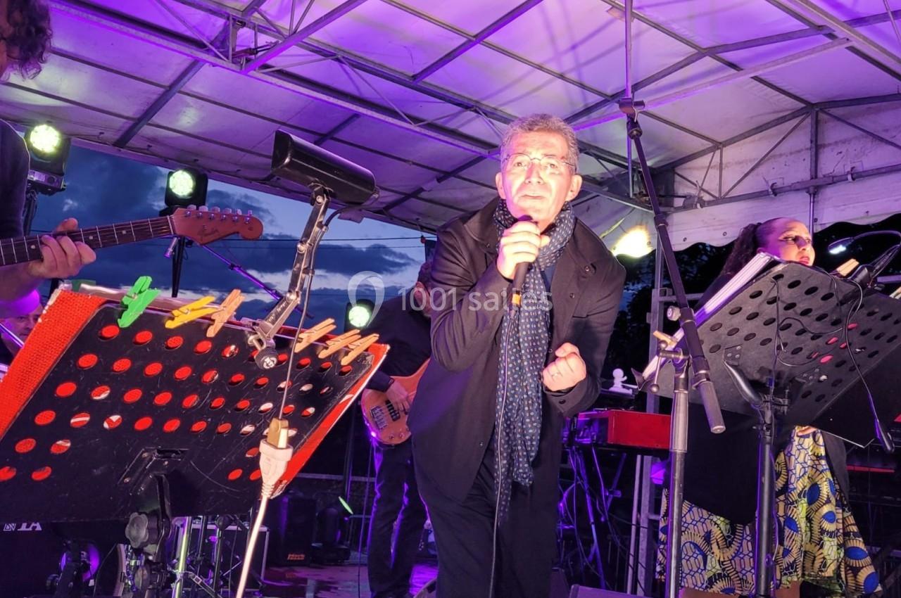 Un chanteur interprète sur scène, micro à la main, entouré de musiciens sous un éclairage violet.