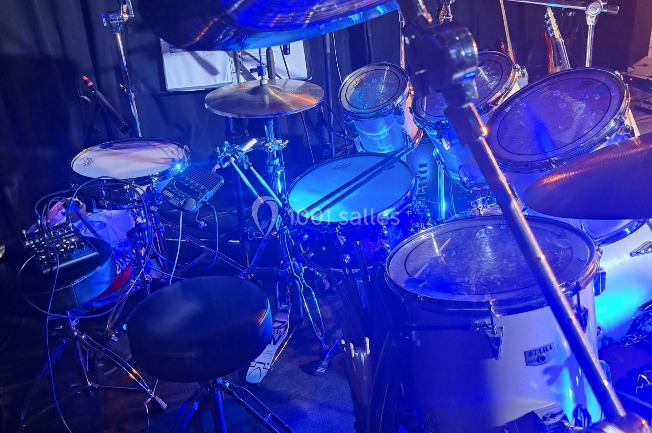 Batterie installée sur une scène avec éclairage bleu, entourée de câbles et d'équipements audio.