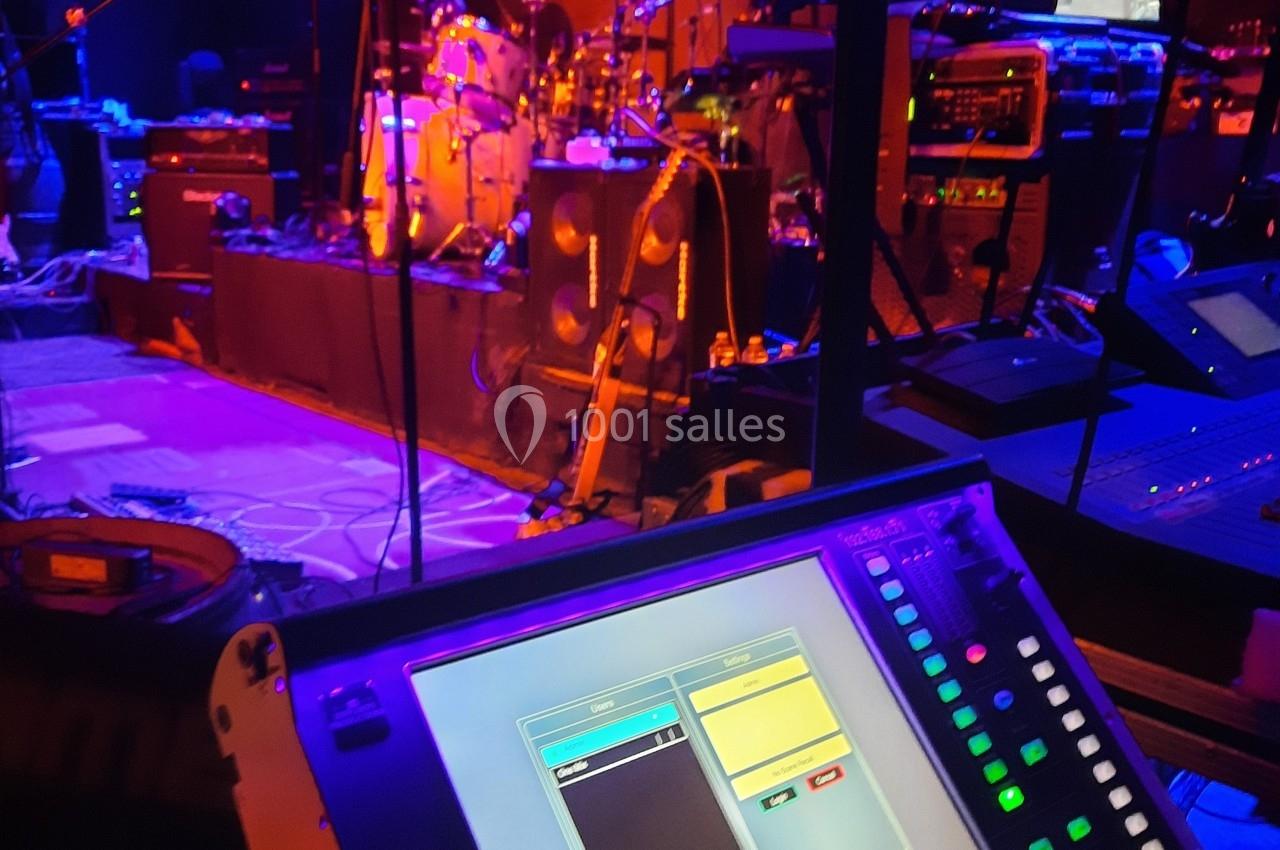 Console de mixage lumineuse au premier plan avec une scène de concert éclairée en arrière-plan.