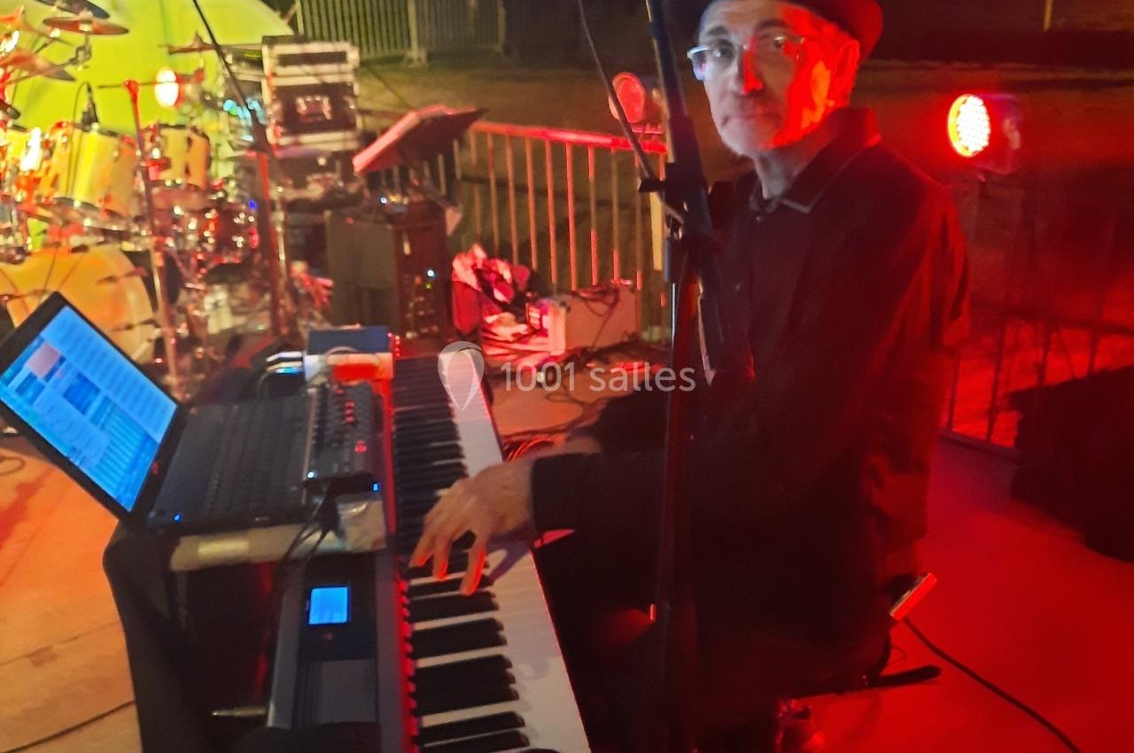 Un musicien joue du clavier sur une scène extérieure éclairée, entouré d'équipements de musique.