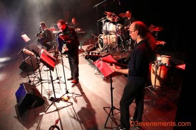 Un groupe de musiciens joue sur scène avec divers instruments, éclairé par des projecteurs.