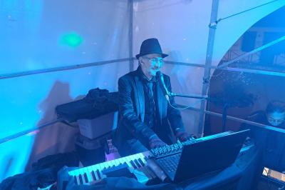 Un batteur joue sur une batterie argentée sur une scène sombre, avec un micro à proximité.