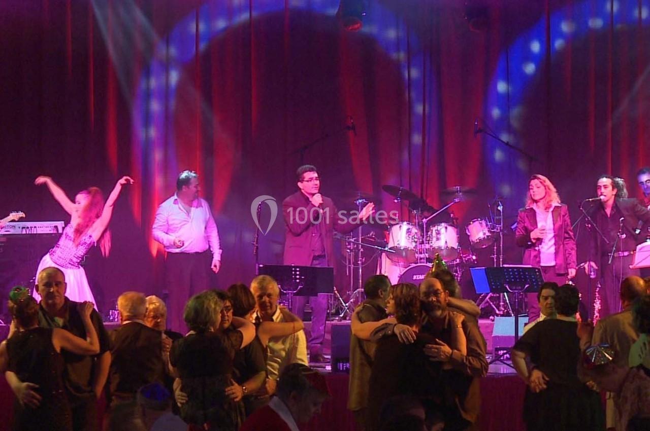 Des personnes dansent devant un groupe de musiciens sur scène, éclairés par des lumières colorées.