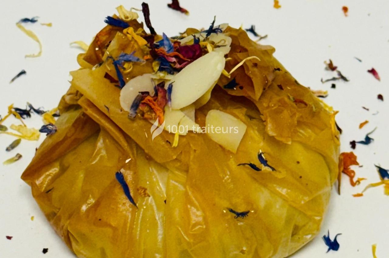 Pochette en tissu jaune contenant des pétales colorés et des morceaux d'amande, posée sur une surface blanche.