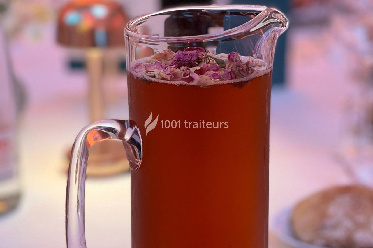 Carafe de boisson rouge ornée de pétales de fleurs séchées, posée sur une table dans un décor lumineux.