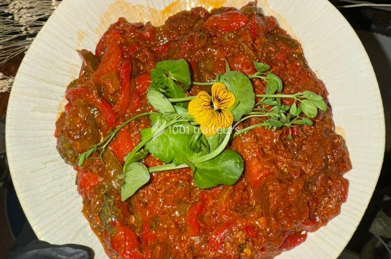 Plat de légumes mijotés avec des poivrons rouges, garni de feuilles fraîches et d'une fleur comestible.