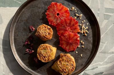 Tranches d'orange garnies de groseilles, pétales de fleurs, amandes effilées et feuilles de menthe dans une assiette.