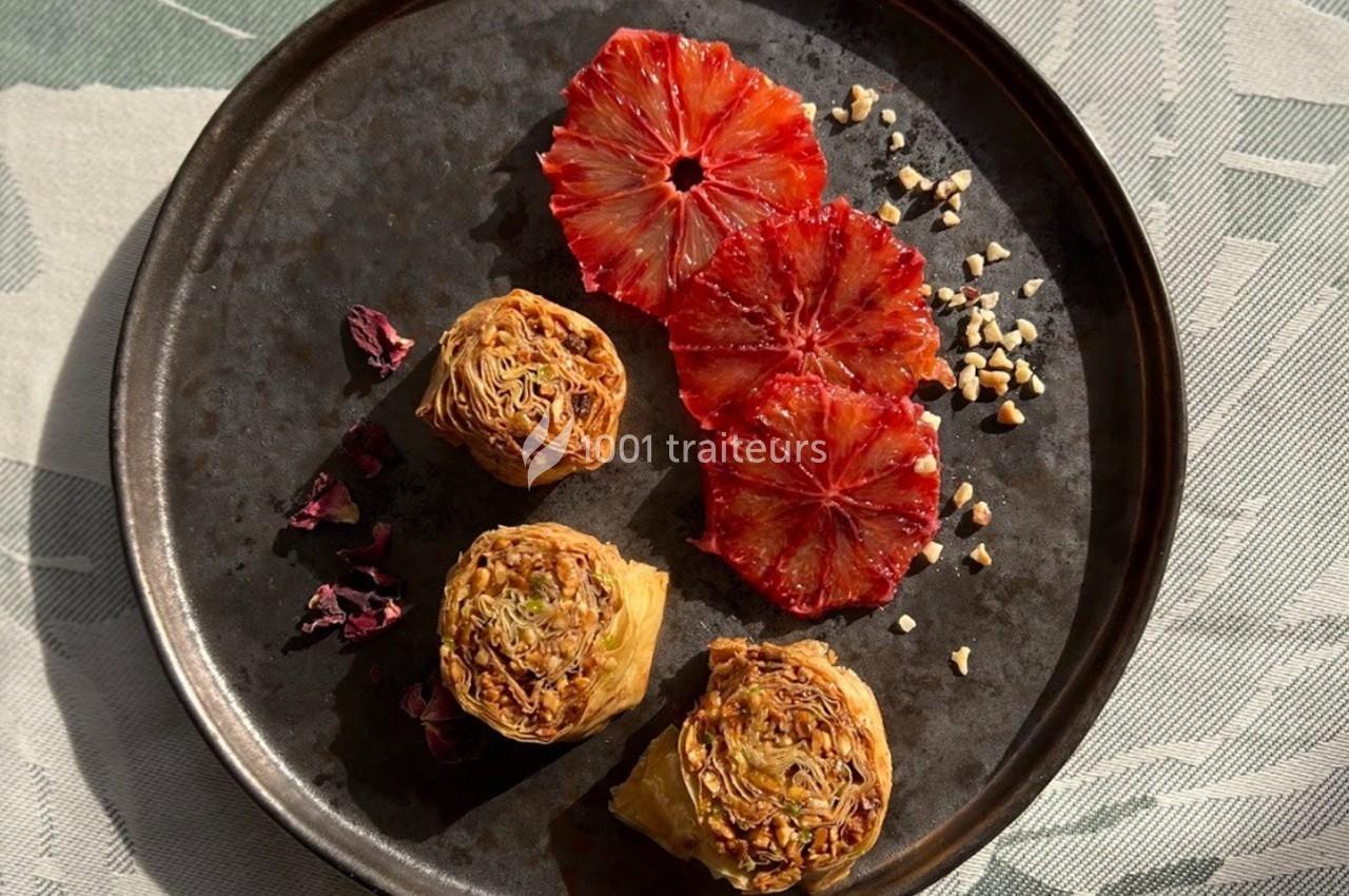 Assiette contenant des rouleaux de pâte dorés, des tranches d'orange sanguine et des éclats de noisettes.