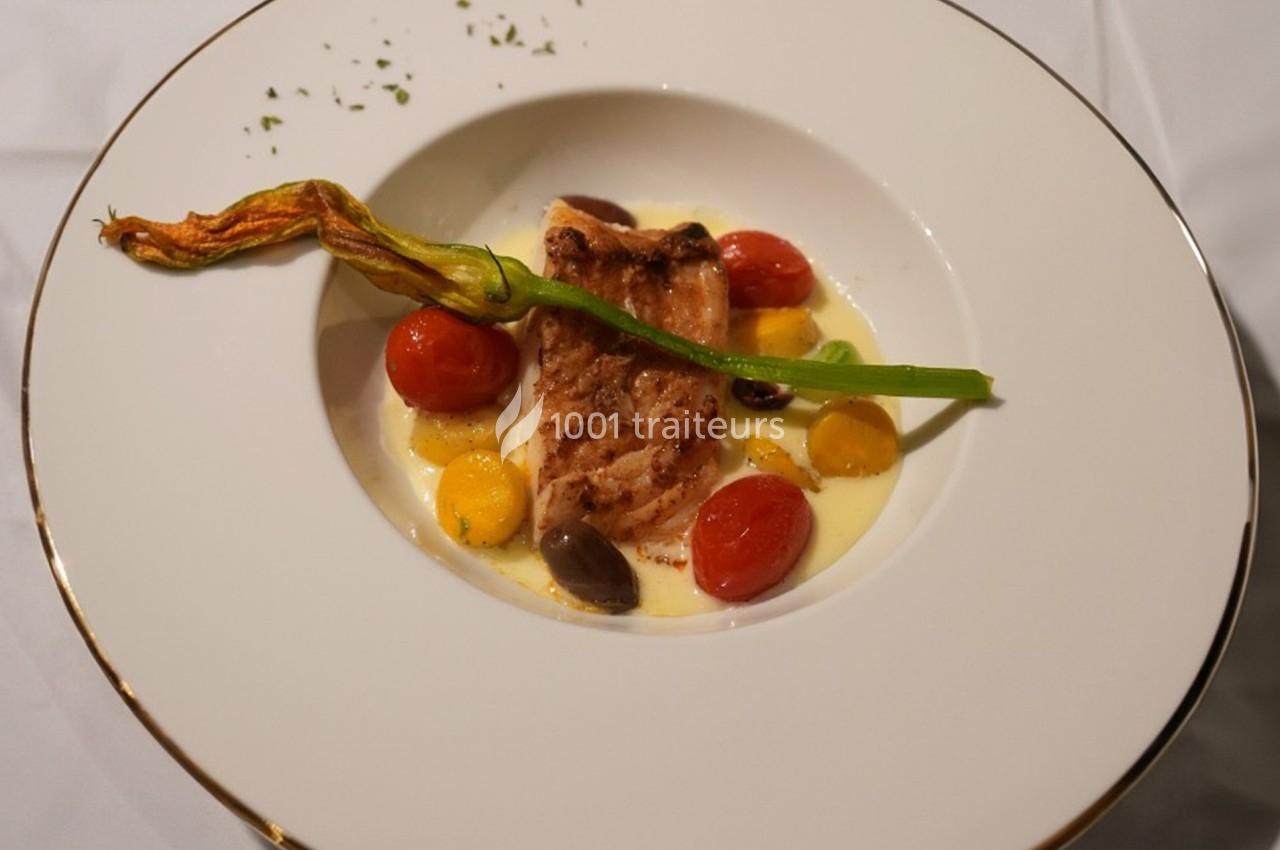 Filet de poisson grillé servi avec des tomates cerises, olives, crème onctueuse et une fleur de courgette en garniture.