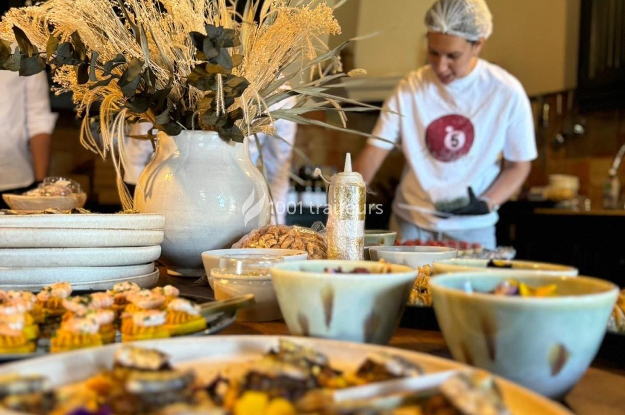 Buffet de plats variés avec une personne en arrière-plan préparant des aliments dans une cuisine.