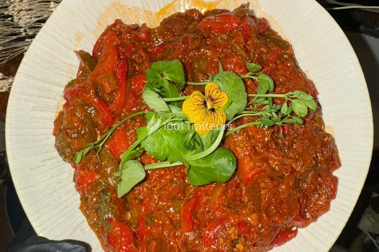 Plat de légumes mijotés avec une sauce rouge, garni de feuilles fraîches et d'une fleur comestible jaune.