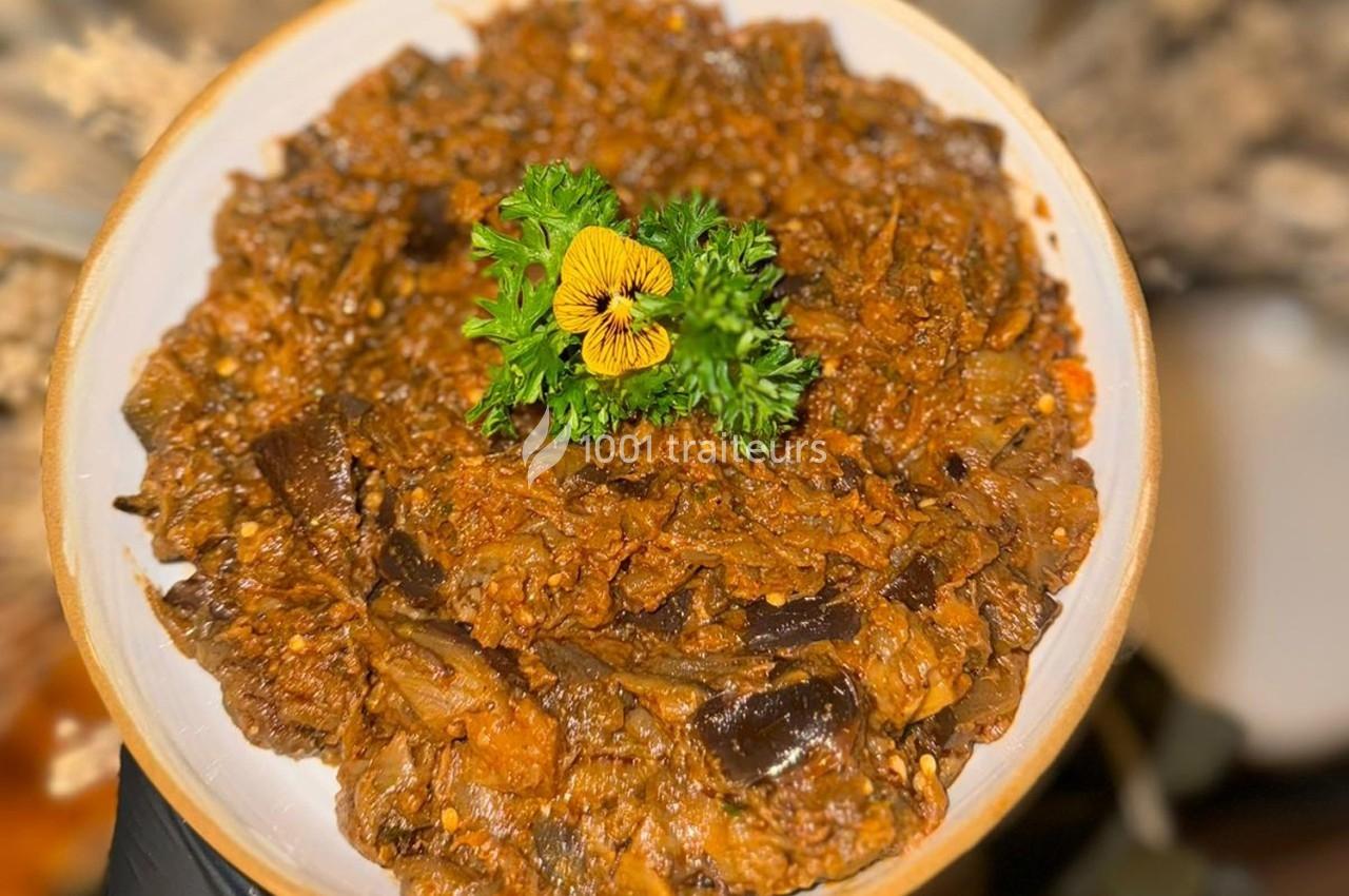 Plat de légumes mijotés avec des aubergines, garni de persil frais et d'une fleur comestible jaune.