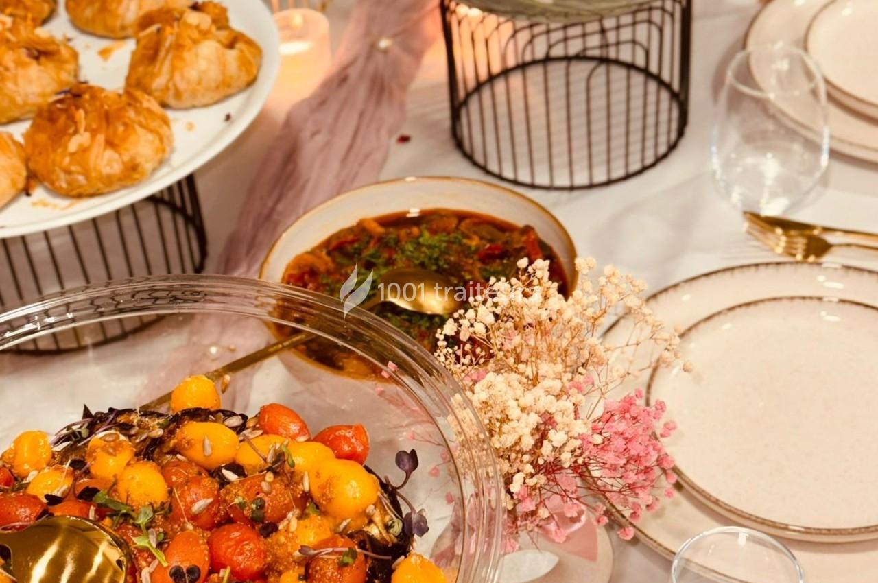 Table dressée avec des plats variés, dont une salade de tomates cerises et un plat mijoté, décorée de fleurs séchées.