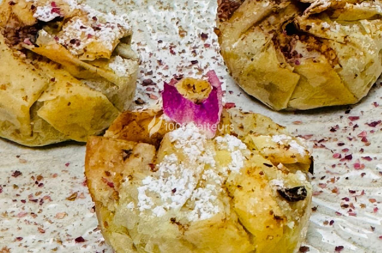 Feuilletés dorés garnis, décorés de sucre glace et de pétales de rose, posés sur une assiette parsemée d'épices.