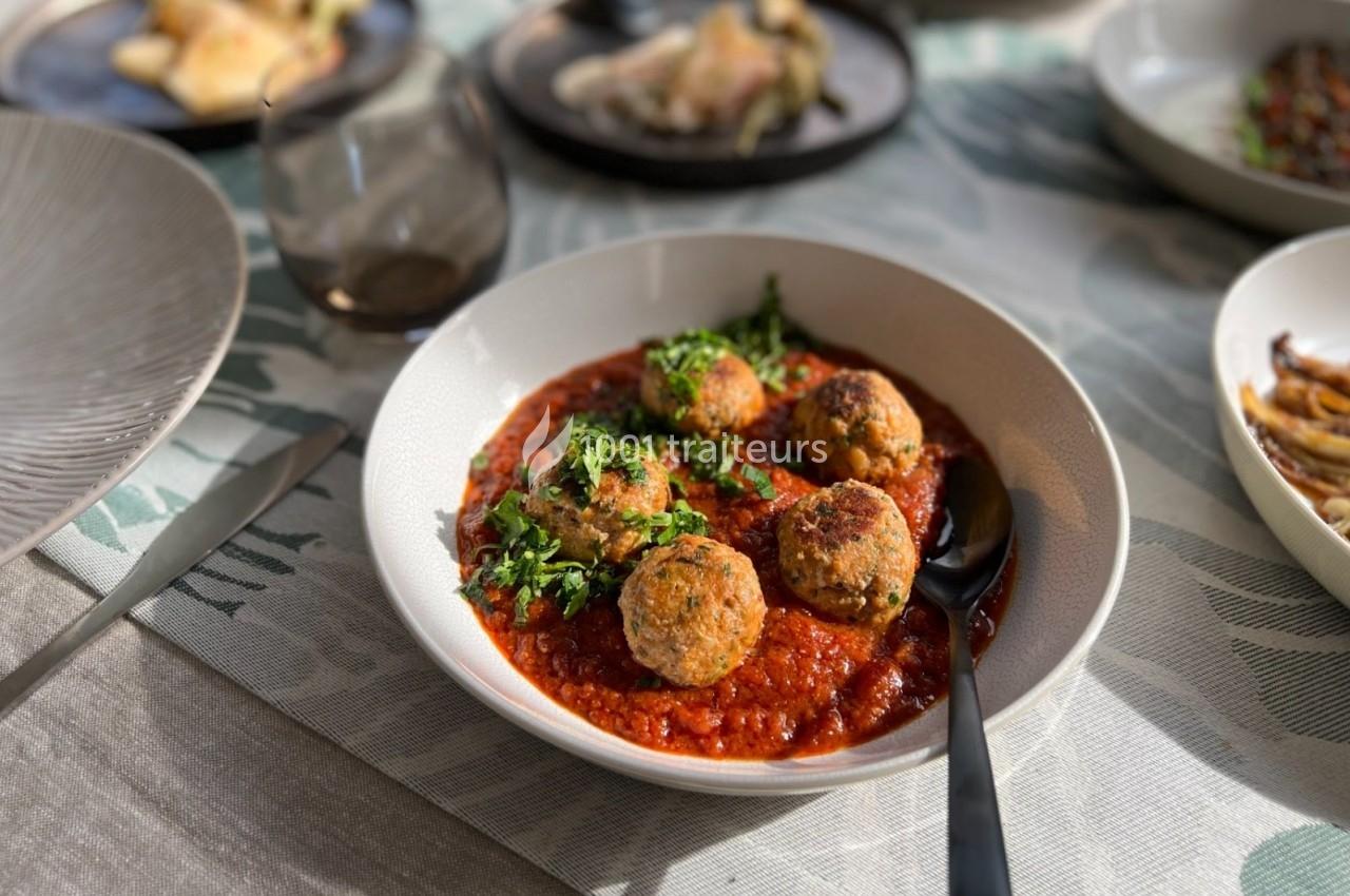 Assiette de boulettes de viande servies sur une sauce tomate, garnies de persil, posée sur une table dressée.