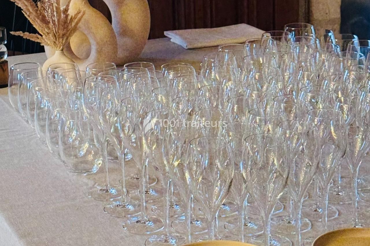 Verres à vin transparents alignés sur une table recouverte d'une nappe beige, avec des décorations en arrière-plan.