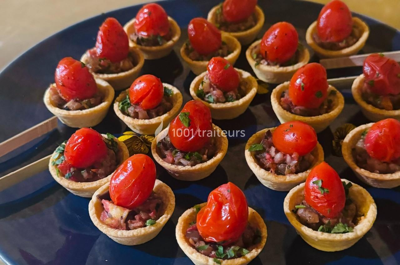 Tartelettes garnies de légumes et surmontées de tomates cerises rôties, disposées sur une assiette sombre.