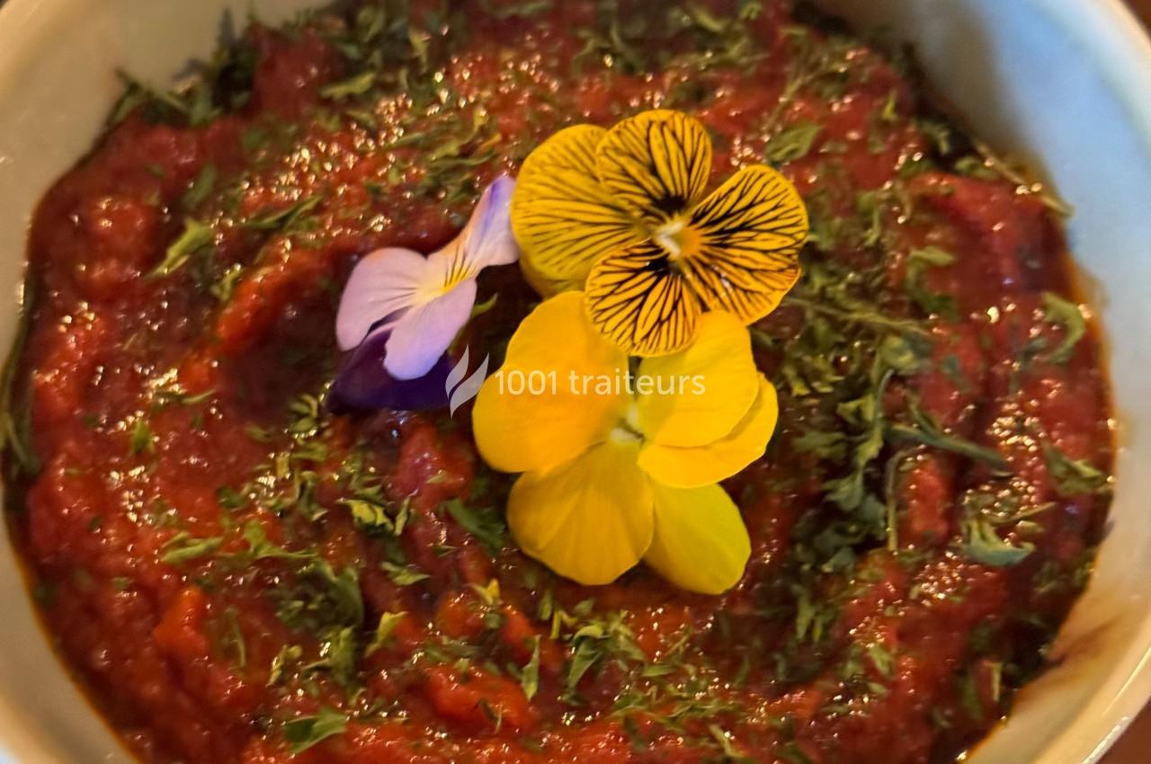 Bol de sauce rouge garnie de fleurs comestibles colorées et de fines herbes hachées.