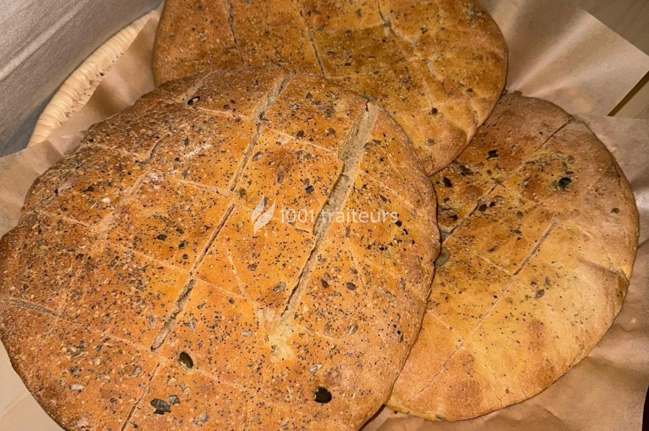 Trois pains ronds dorés, parsemés de graines, disposés dans un panier recouvert de papier brun.