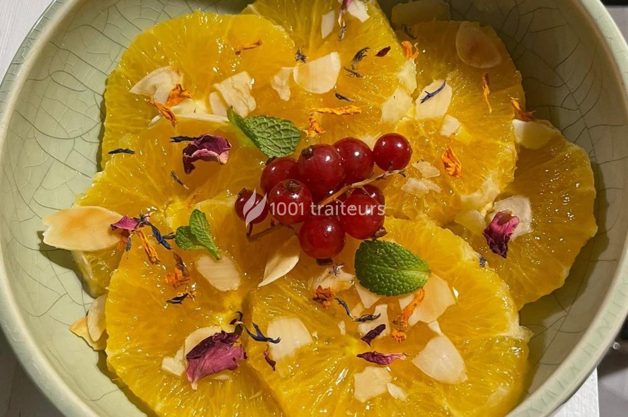 Tranches d'orange garnies de groseilles, pétales de fleurs, amandes effilées et feuilles de menthe dans une assiette.