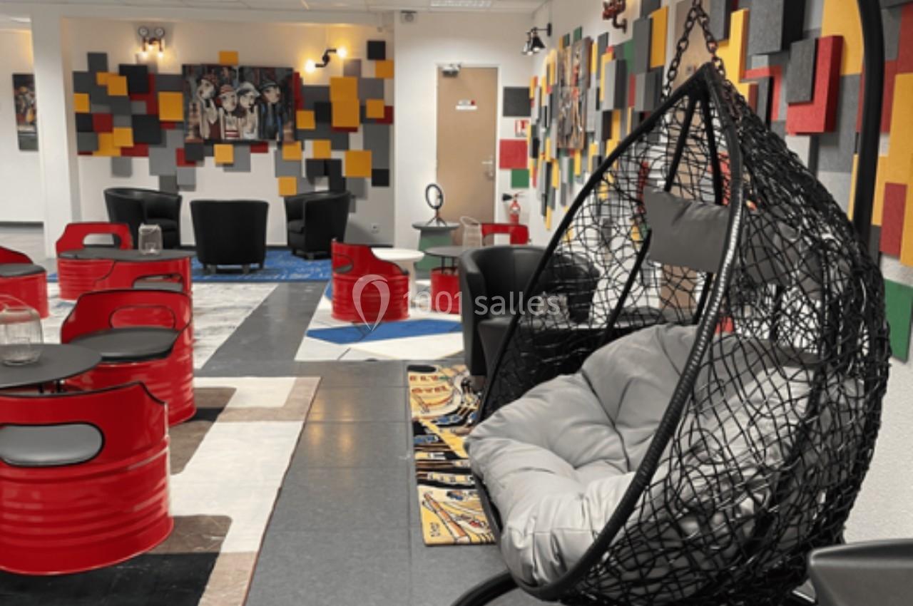 Espace intérieur moderne avec fauteuil suspendu, tables rouges en tonneaux et décorations murales colorées.