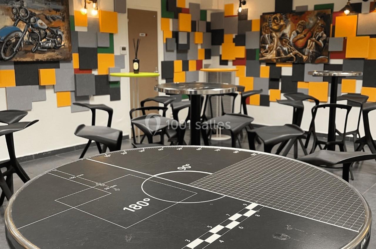 Salle moderne avec tables hautes, chaises noires et murs décorés de panneaux colorés et tableaux.