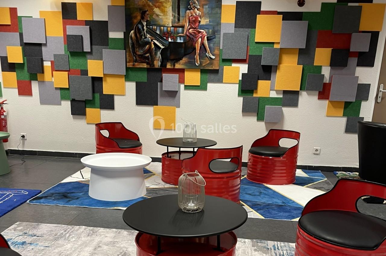 Espace lounge avec fauteuils rouges, tables basses noires et blanches, décor coloré et tableau mural.