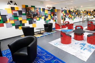 Espace de pause avec comptoir noir, décorations murales, tableau coloré et éclairage chaleureux.