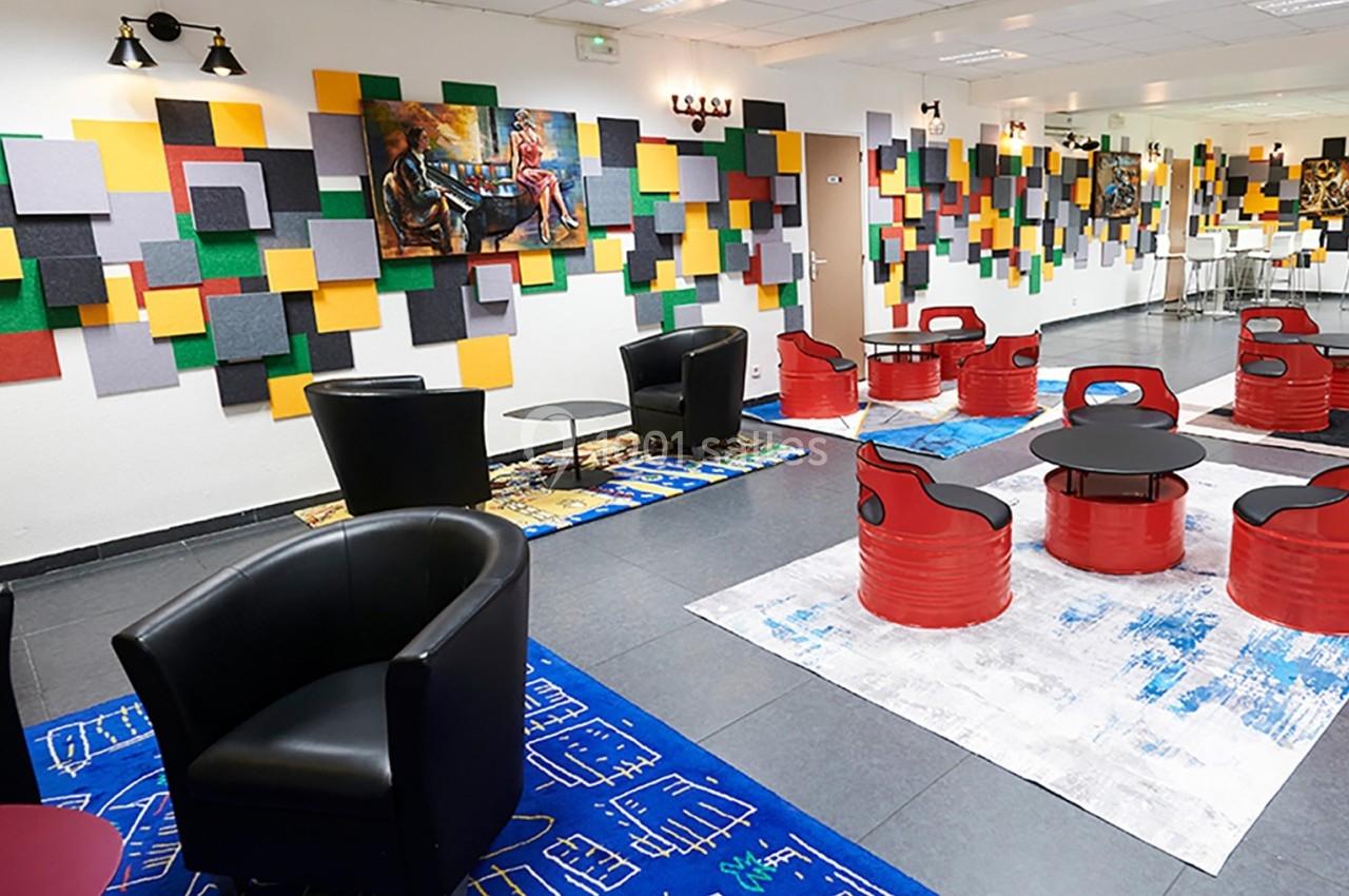 Espace intérieur moderne avec fauteuils noirs, tables rouges, tapis colorés et murs décorés de panneaux acoustiques.