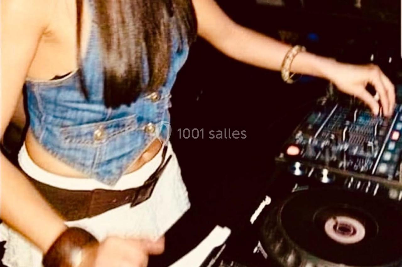 Une femme mixant de la musique sur une table de mixage, vêtue d'un haut en jean et d'une jupe claire.