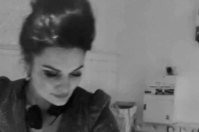 Femme concentrée, portant une robe claire, devant un mur en pierre texturée sous un éclairage violet.