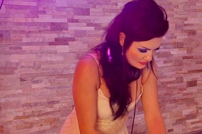 Femme concentrée, portant une robe claire, devant un mur en pierre texturée sous un éclairage violet.