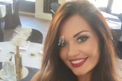 Femme souriante avec des cheveux bruns, maquillage soigné, dans une salle décorée avec des tables dressées.