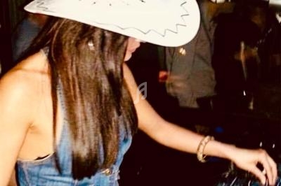 Femme portant un chapeau blanc et une tenue en jean, manipulant un équipement dans un environnement sombre.