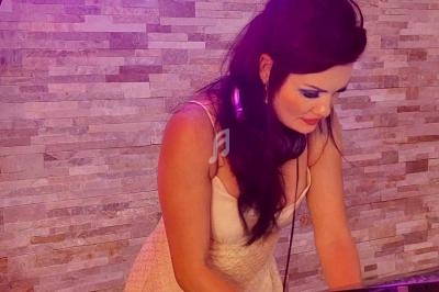 Femme portant un casque audio, concentrée sur un équipement de mixage, devant un mur en pierre beige.