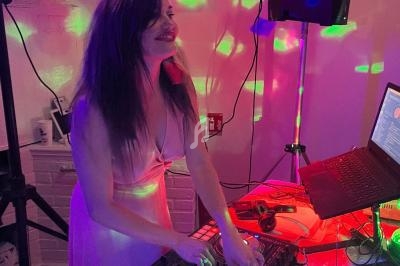 Femme en robe rose mixant de la musique sur une table de mixage dans une ambiance lumineuse colorée.
