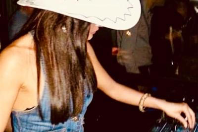 Salle décorée pour un événement avec tables blanches, chaises couvertes, guirlandes lumineuses et bouquets de fleurs.
