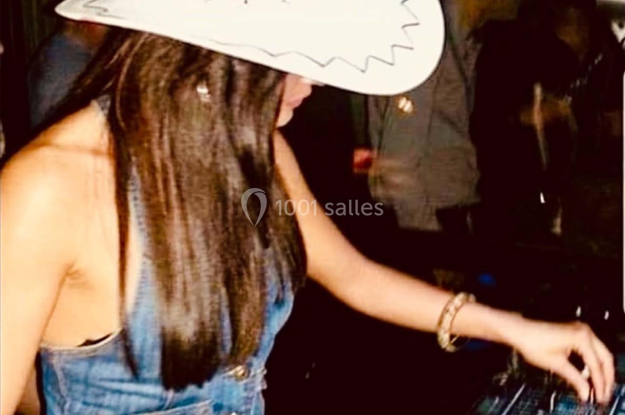 Femme portant un chapeau blanc et une tenue en jean, manipulant des équipements sur une table dans un environnement sombre.