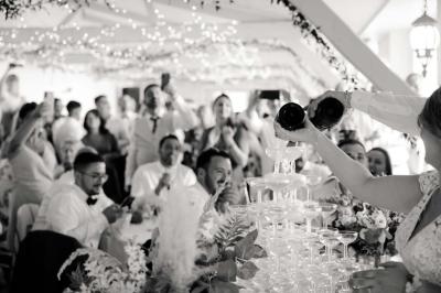 Salle décorée pour un événement avec tables blanches, chaises couvertes, guirlandes lumineuses et bouquets de fleurs.