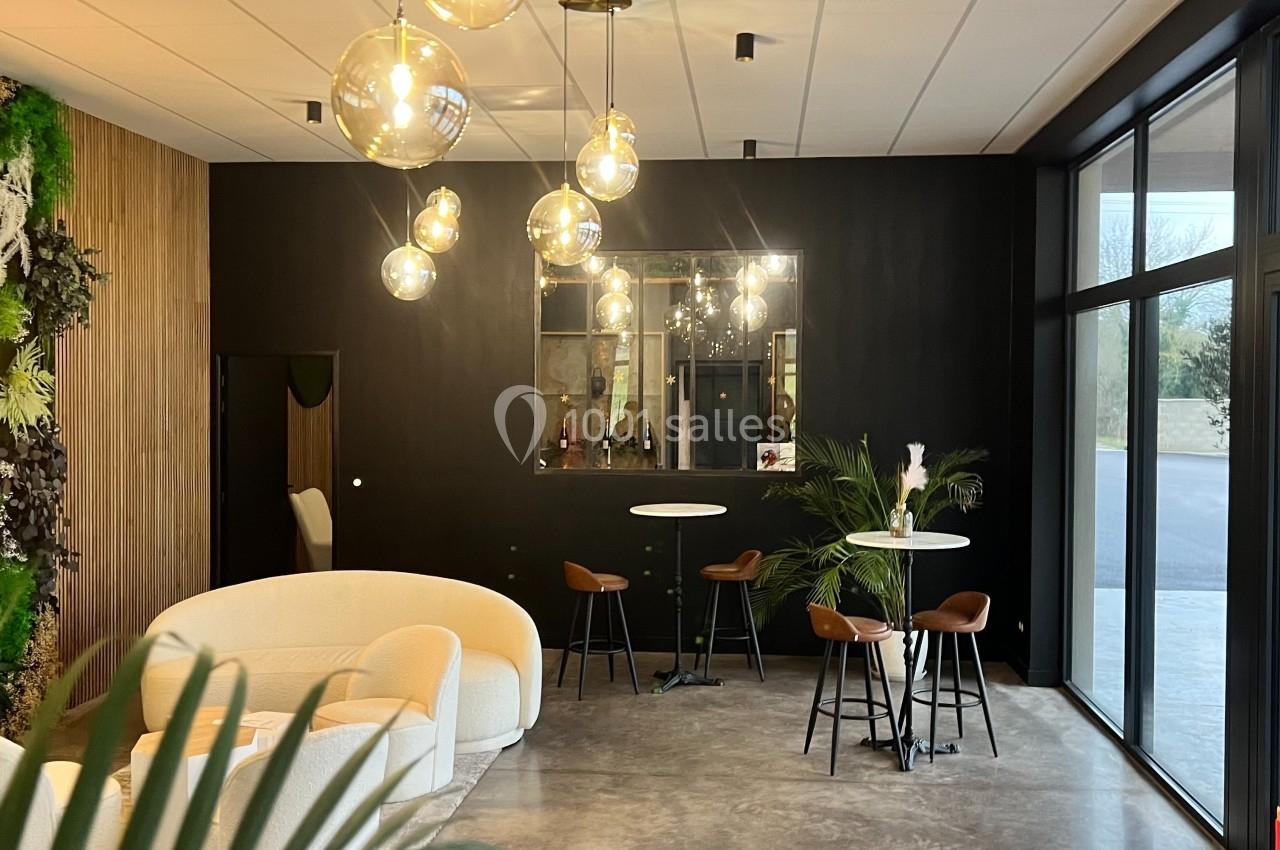 Espace intérieur moderne avec canapé beige, tables hautes, plantes et luminaires suspendus dans une ambiance lumineuse.