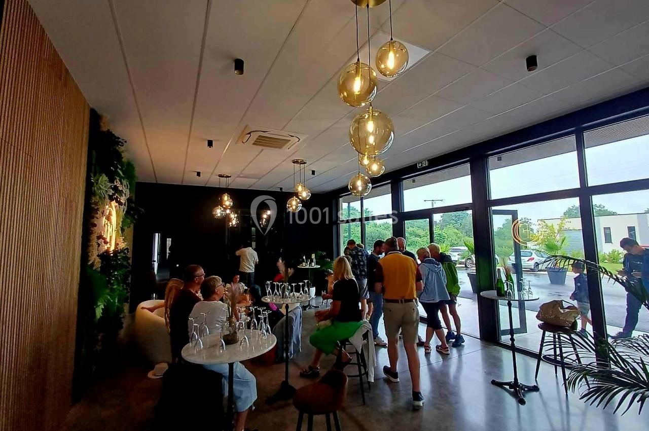 Groupe de personnes discutant dans un espace moderne avec des tables, des plantes et des luminaires suspendus.