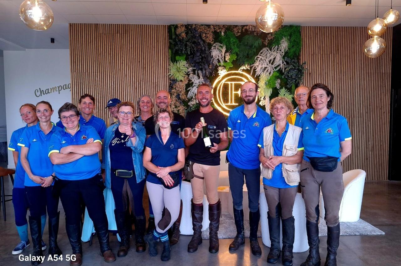Un groupe de personnes en tenue d'équitation pose dans un espace intérieur décoré de plantes et de bois.