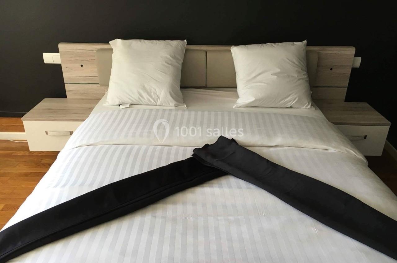 Lit double avec draps blancs, deux oreillers et une décoration en tissu noir pliée en forme de V.