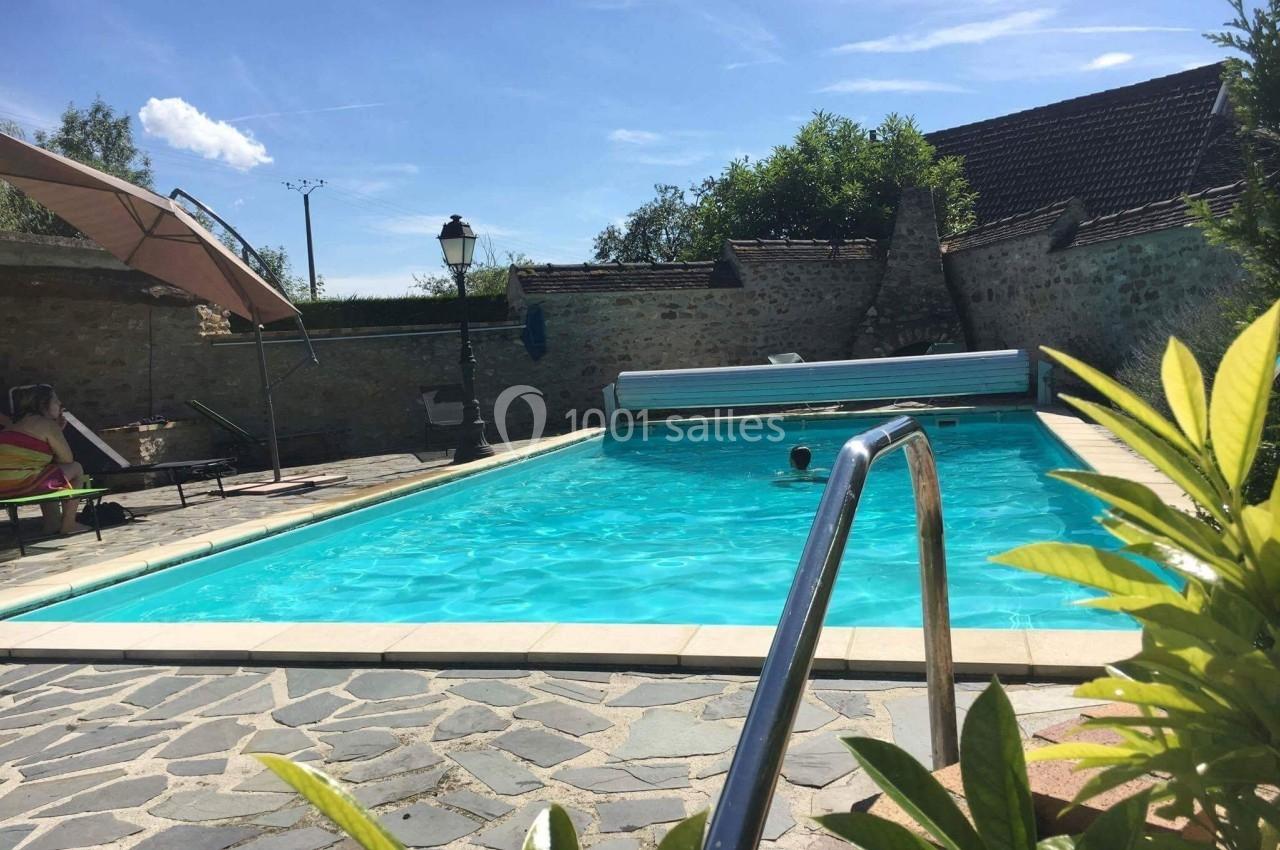Piscine extérieure entourée de pierres et de végétation, avec une personne nageant sous un ciel ensoleillé.