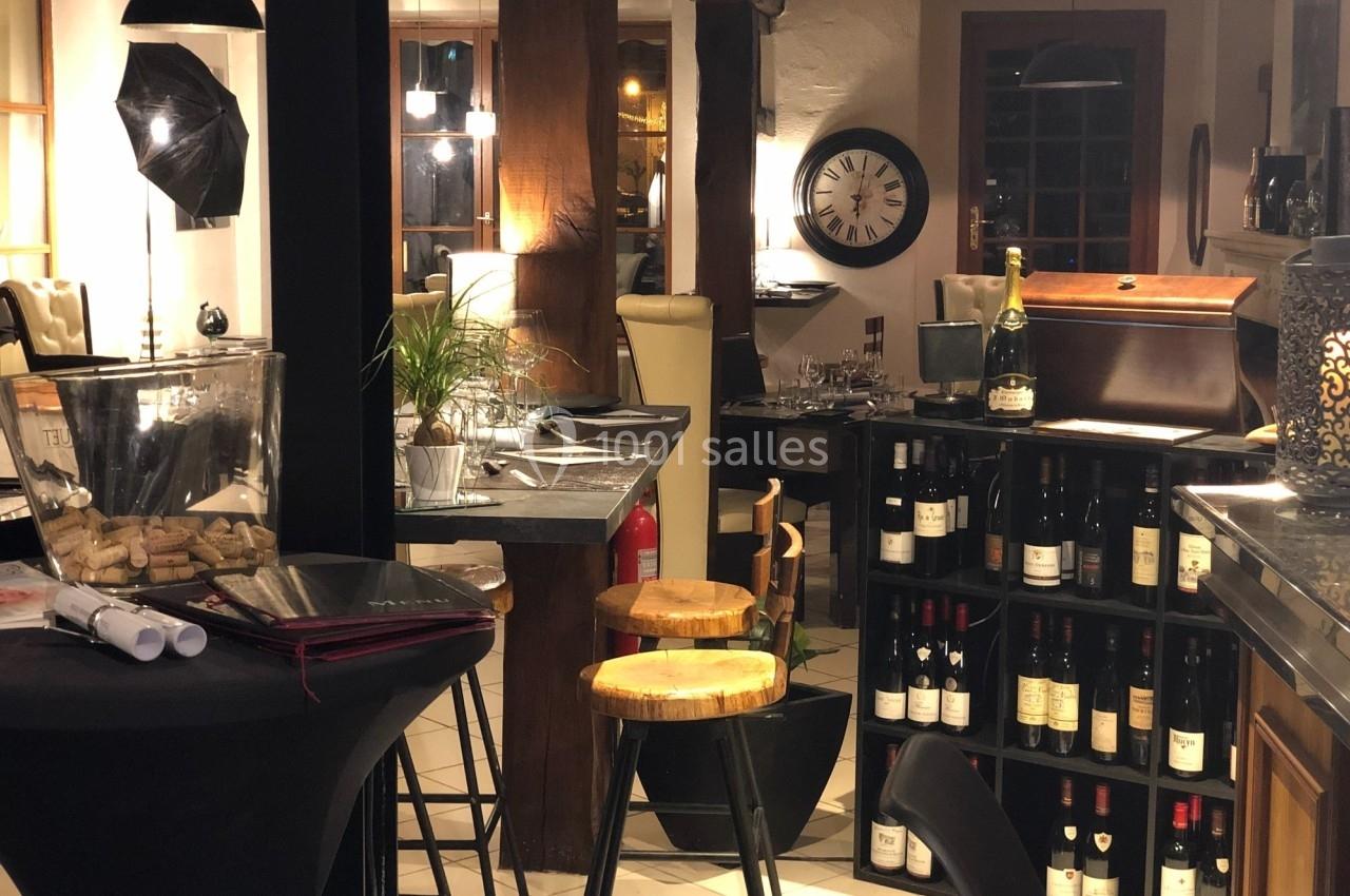 Intérieur d'un bar ou restaurant avec des tables hautes, des bouteilles de vin exposées et une ambiance chaleureuse.