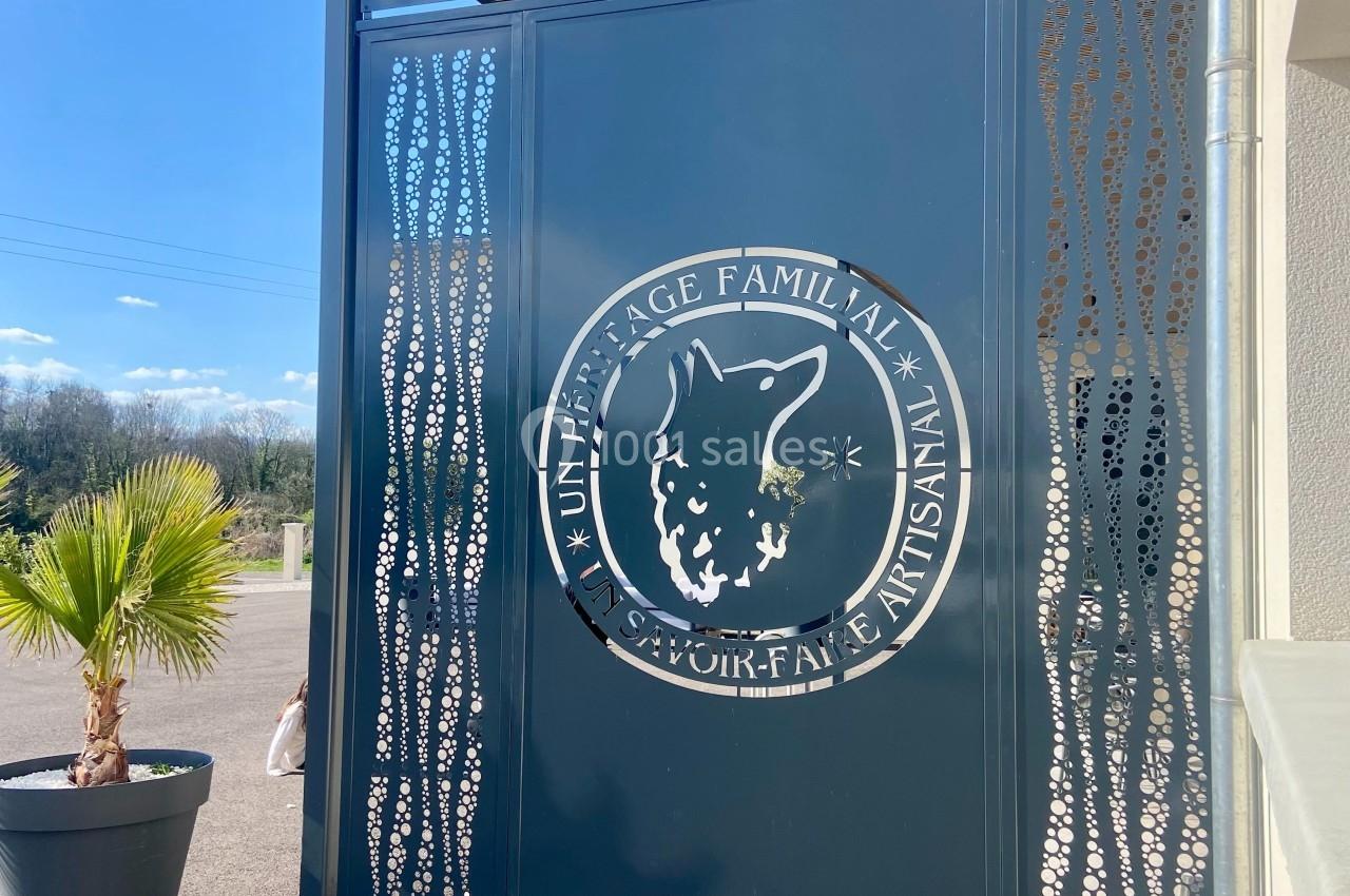 Portail métallique avec le logo d'un loup et l'inscription ’Un héritage familial, savoir-faire artisanal’, près d'une plante.