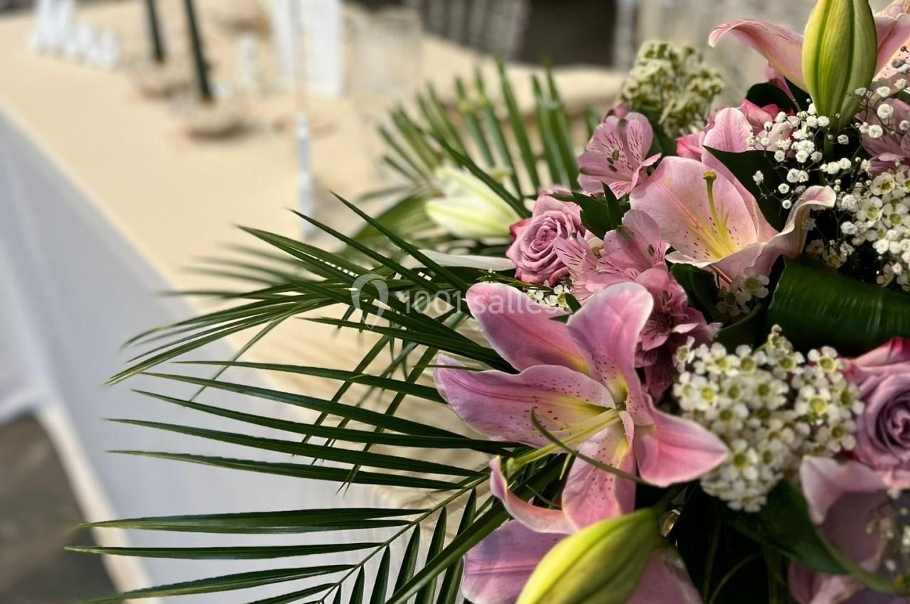 Bouquet de fleurs roses, blanches et vertes avec des lys, des roses et du gypsophile, posé près d'une table beige.