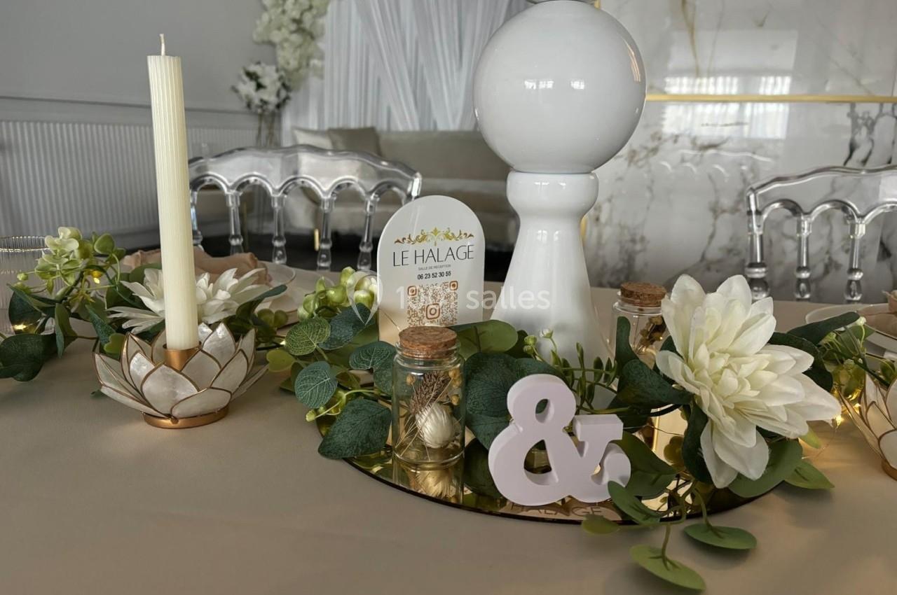 Centre de table décoratif avec fleurs blanches, feuillage, bougies et éléments décoratifs sur un plateau doré.