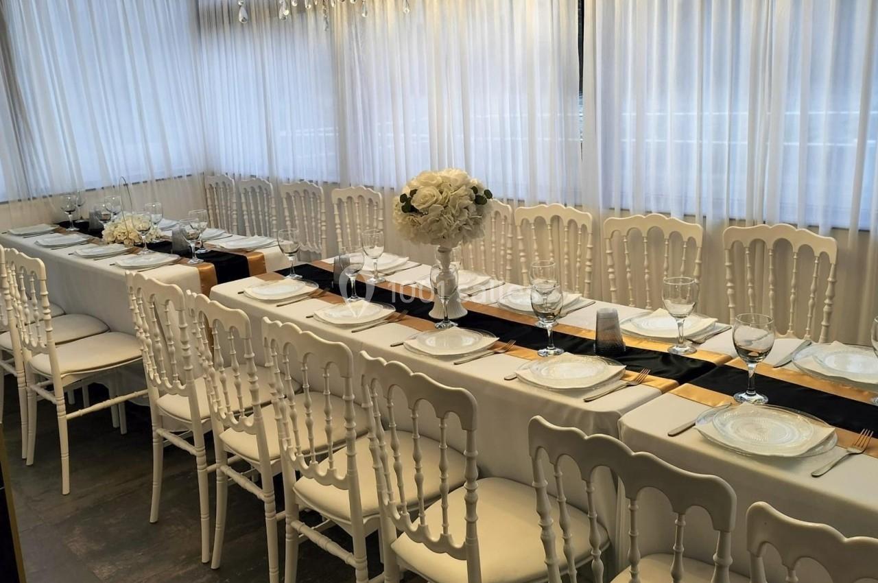 Table dressée avec vaisselle blanche, verres et centres de table fleuris, entourée de chaises blanches dans une salle…