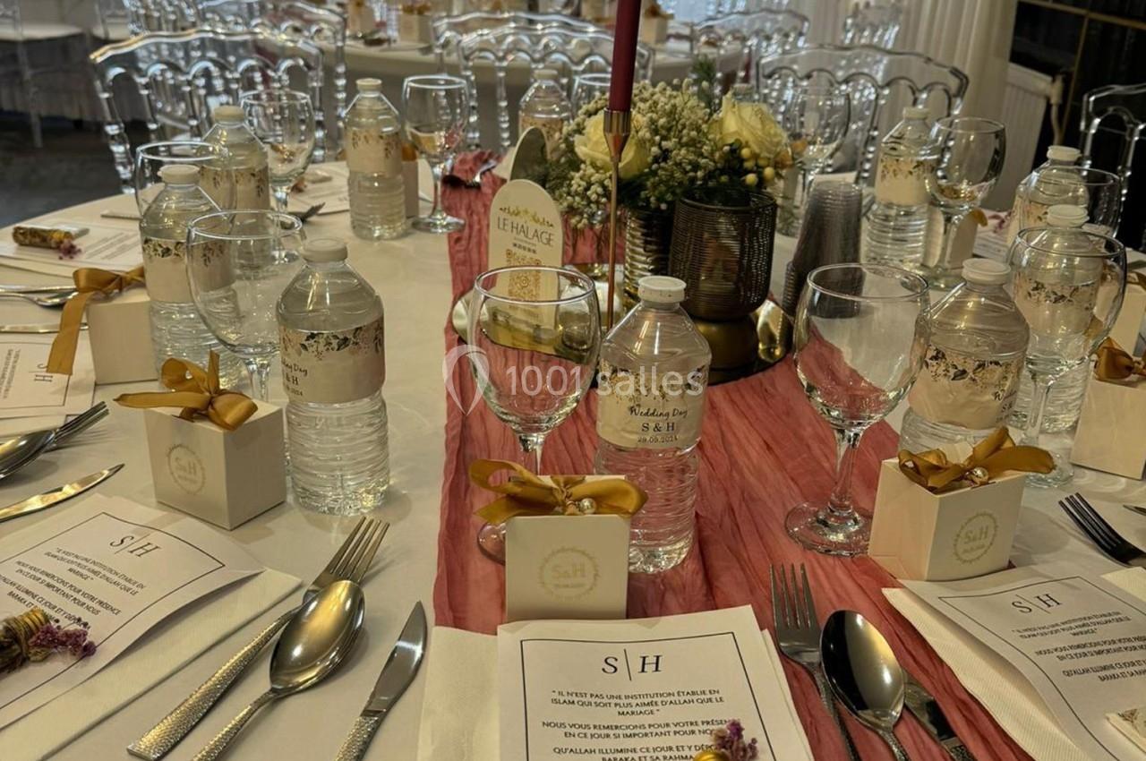 Table dressée pour un événement avec nappes blanches, décorations élégantes, menus, bouteilles d'eau et cadeaux invités.